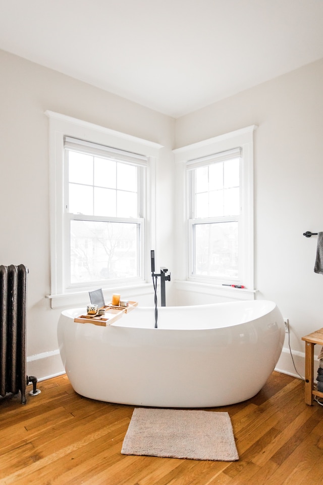 bathroom with a freestanding tub, radiator heating unit, baseboards, and wood finished floors