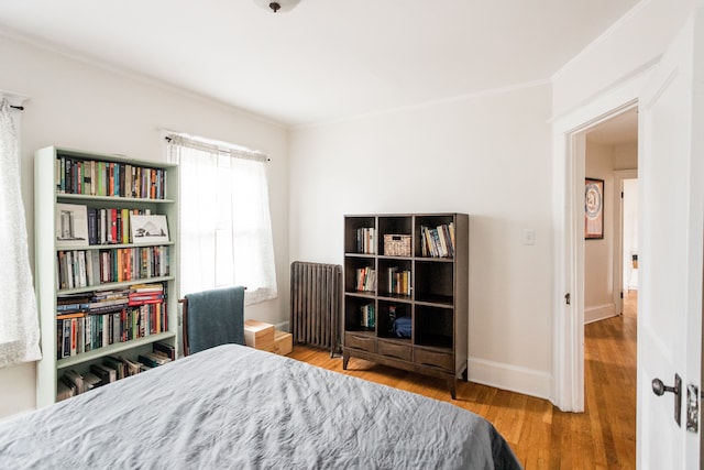 bedroom featuring crown molding, radiator heating unit, baseboards, and wood finished floors