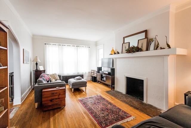 living room featuring radiator, arched walkways, a tile fireplace, crown molding, and light wood-type flooring