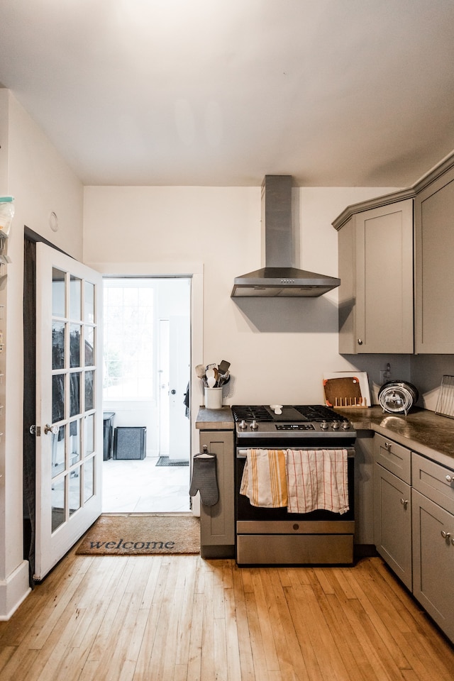 kitchen featuring light wood finished floors, gray cabinets, stainless steel gas range, and wall chimney range hood