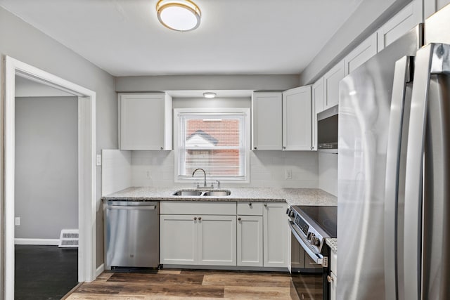 kitchen featuring wood finished floors, a sink, white cabinets, appliances with stainless steel finishes, and backsplash