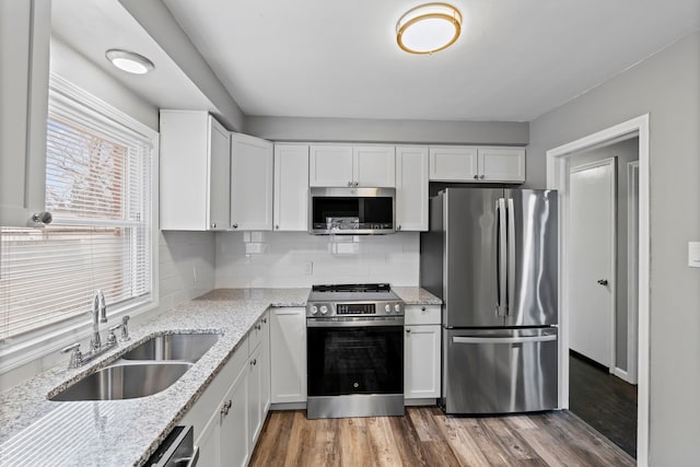 kitchen featuring wood finished floors, white cabinetry, stainless steel appliances, and a sink