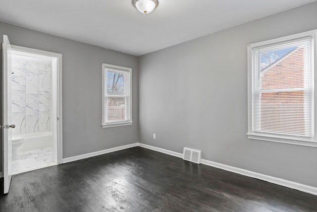 empty room featuring visible vents, baseboards, and dark wood-style flooring