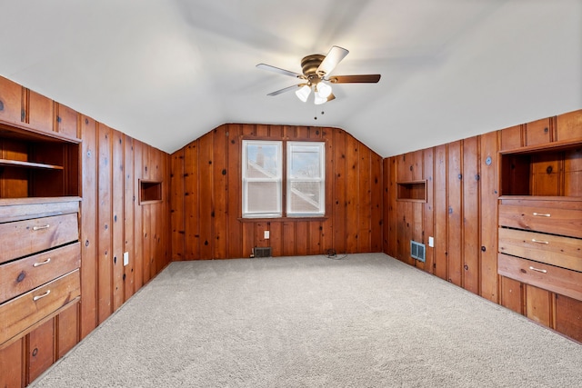 additional living space with visible vents, lofted ceiling, carpet floors, and wood walls