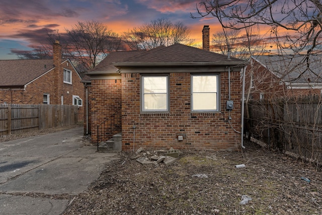 exterior space featuring brick siding, a chimney, a fenced backyard, and a shingled roof