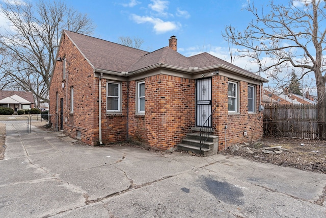 view of front of house featuring fence, brick siding, roof with shingles, and a chimney