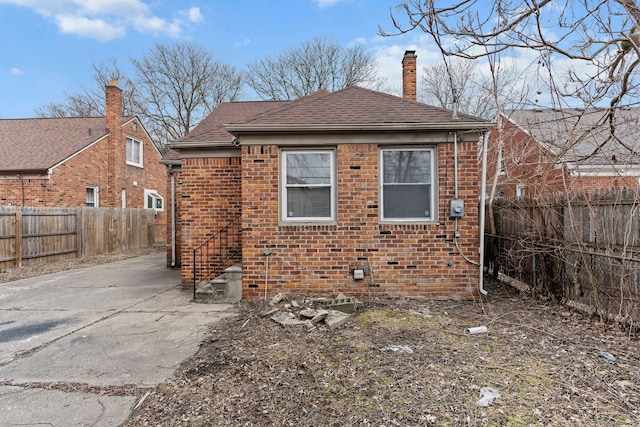 back of house featuring brick siding, a chimney, a fenced backyard, and a shingled roof