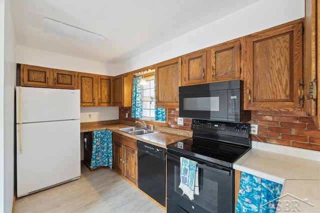 kitchen featuring brown cabinets, black appliances, a sink, light wood-style floors, and light countertops