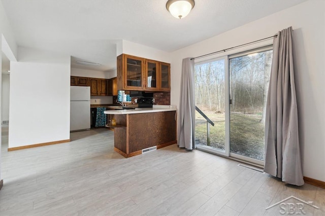 kitchen featuring visible vents, glass insert cabinets, a peninsula, and freestanding refrigerator