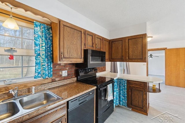 kitchen with black appliances, a sink, a textured ceiling, a peninsula, and brown cabinetry