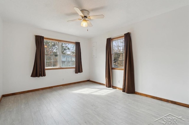 spare room featuring baseboards, light wood-style floors, a ceiling fan, and a textured ceiling