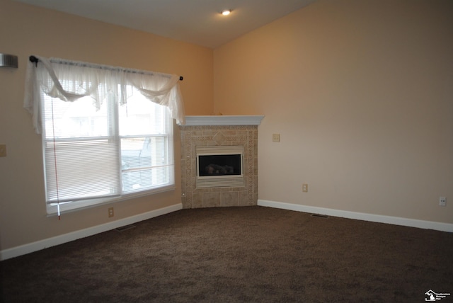 unfurnished living room featuring baseboards, visible vents, vaulted ceiling, a tiled fireplace, and dark carpet