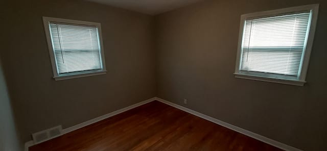 empty room featuring dark wood finished floors, plenty of natural light, baseboards, and visible vents