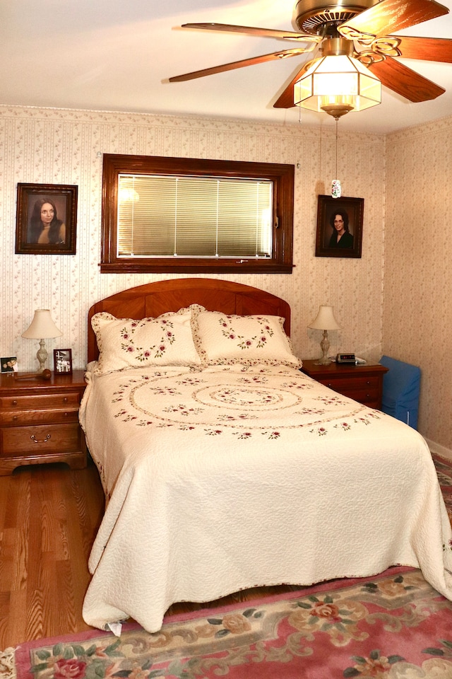 bedroom with wallpapered walls, wood finished floors, and a ceiling fan