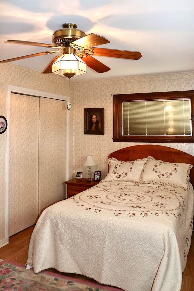 bedroom featuring wallpapered walls, wood finished floors, a closet, and a ceiling fan