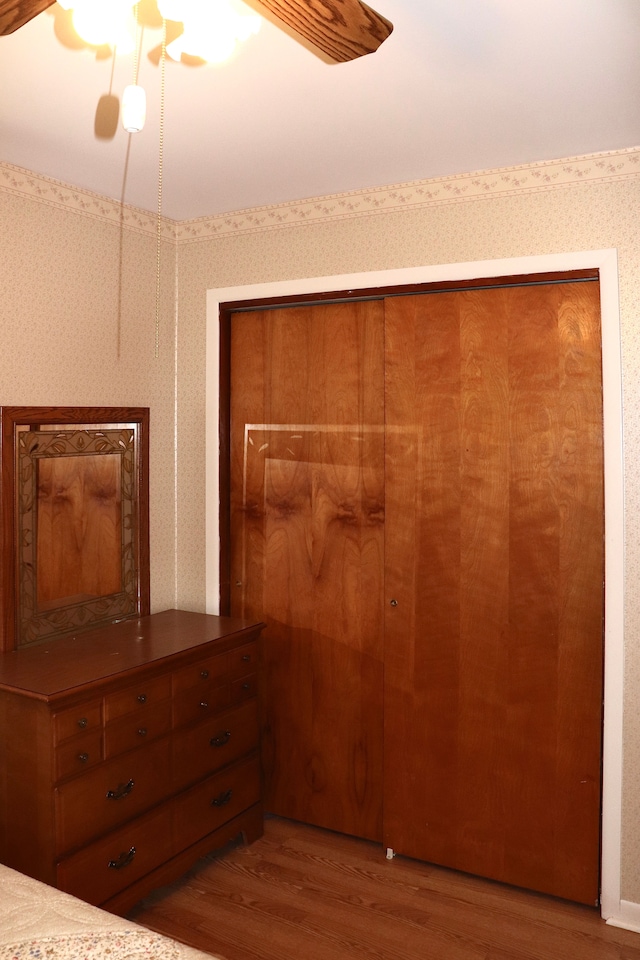 unfurnished bedroom with a closet, wood finished floors, a ceiling fan, and wallpapered walls