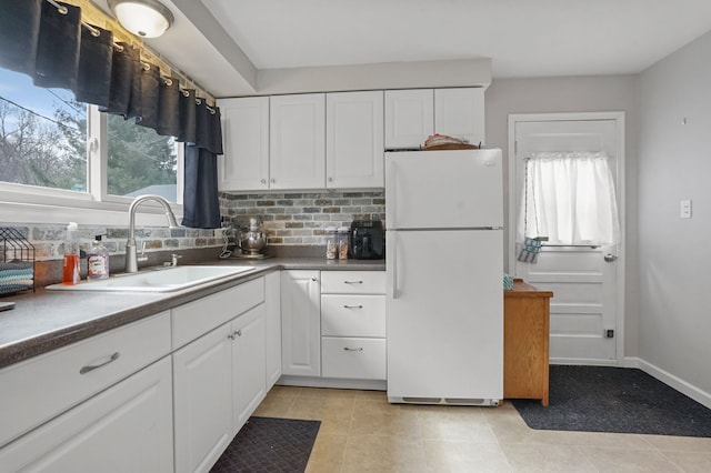 kitchen with backsplash, white cabinets, freestanding refrigerator, and a sink