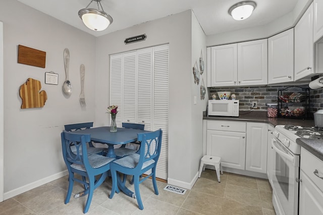 kitchen featuring visible vents, dark countertops, white cabinetry, white appliances, and decorative backsplash