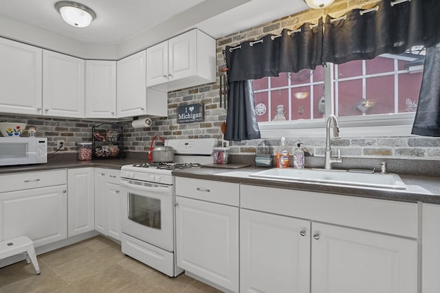 kitchen with white appliances, a sink, decorative backsplash, white cabinetry, and dark countertops