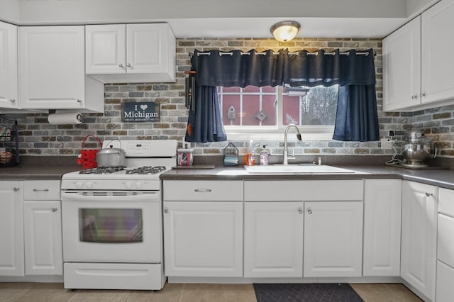 kitchen with dark countertops, white cabinetry, gas range gas stove, and a sink