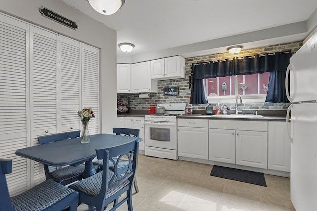 kitchen with a sink, dark countertops, white appliances, white cabinets, and decorative backsplash