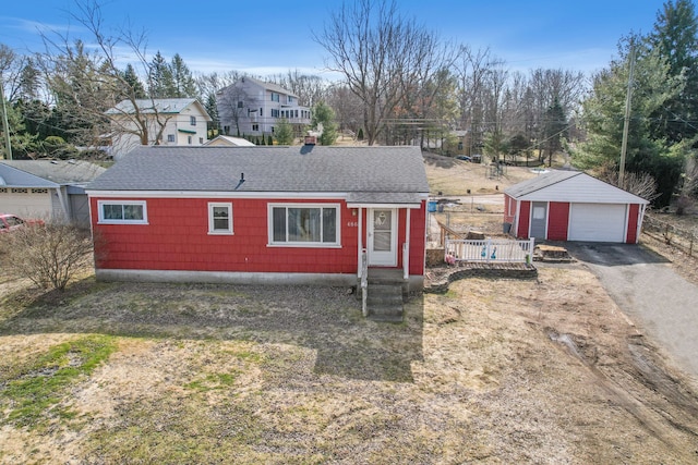 view of front facade with a detached garage, an outbuilding, driveway, and a shingled roof