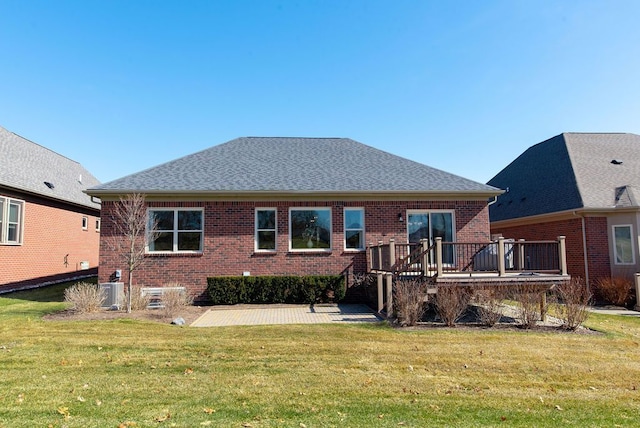 back of property with a lawn, a patio, a shingled roof, a wooden deck, and brick siding