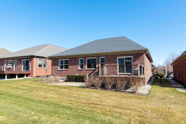 back of property featuring brick siding, a shingled roof, and a yard