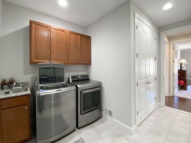 laundry area featuring independent washer and dryer, a sink, cabinet space, light tile patterned floors, and baseboards