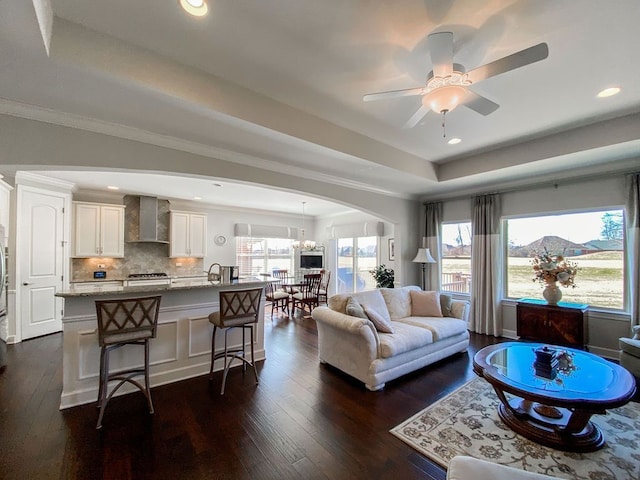 living area with arched walkways, dark wood-style floors, recessed lighting, and a raised ceiling