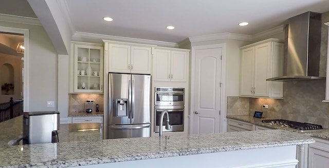 kitchen with light stone counters, stainless steel appliances, glass insert cabinets, crown molding, and wall chimney exhaust hood