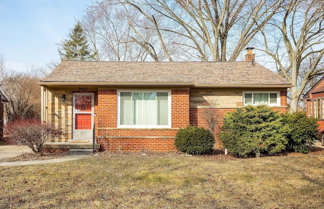 view of front of home with a shingled roof, a front lawn, brick siding, and a chimney