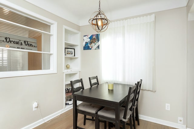 dining space featuring a notable chandelier, built in shelves, wood finished floors, and baseboards