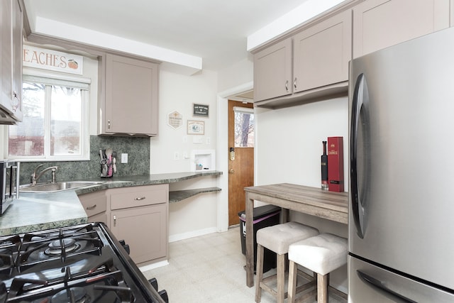 kitchen with a sink, backsplash, freestanding refrigerator, light floors, and black range with gas cooktop