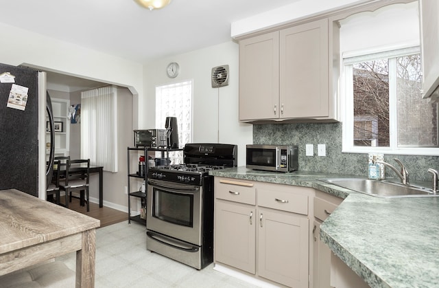 kitchen with tasteful backsplash, baseboards, light floors, appliances with stainless steel finishes, and a sink