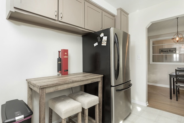 kitchen featuring gray cabinetry, baseboards, light floors, a kitchen bar, and freestanding refrigerator