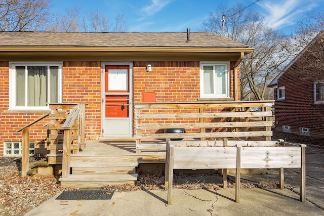 view of front of home with brick siding, a deck, and roof with shingles