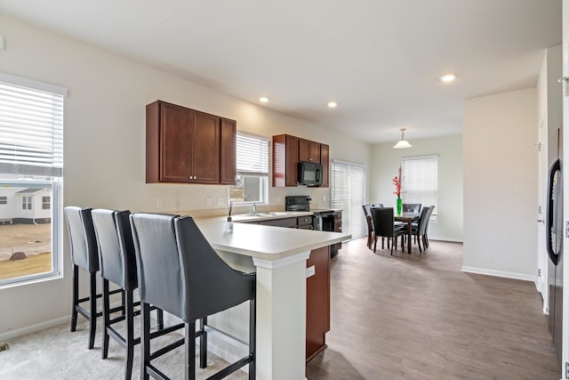 kitchen featuring a kitchen bar, range with electric stovetop, recessed lighting, black microwave, and light countertops