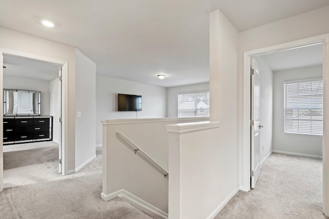 corridor featuring an upstairs landing, baseboards, and light carpet