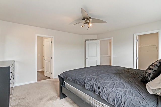 carpeted bedroom featuring a walk in closet, a ceiling fan, and baseboards