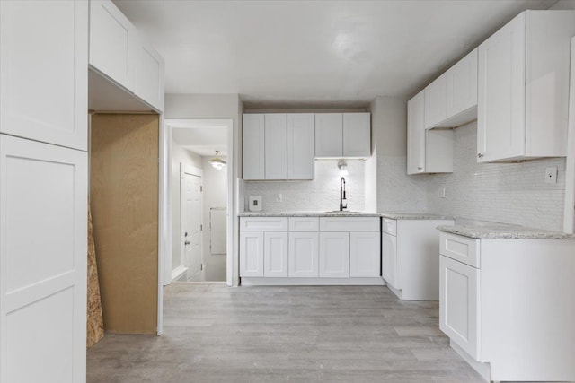 kitchen with a sink, light wood-type flooring, decorative backsplash, and white cabinetry