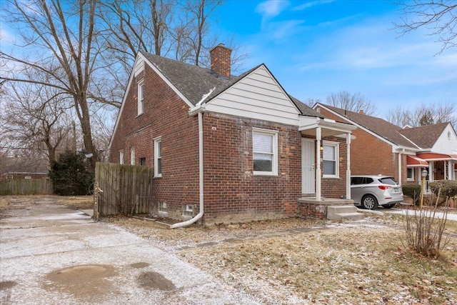 bungalow with brick siding, roof with shingles, a chimney, and fence