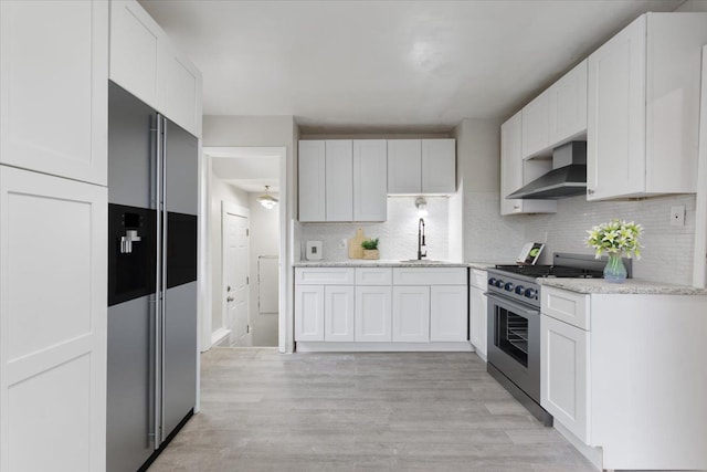 kitchen featuring wall chimney range hood, stainless steel appliances, light wood-style floors, white cabinetry, and a sink