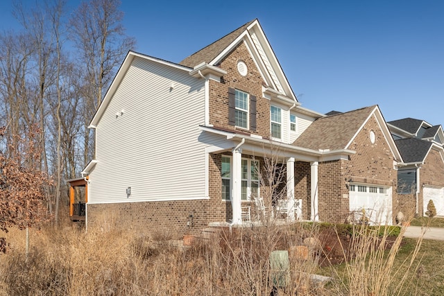 exterior space featuring driveway, a shingled roof, covered porch, a garage, and brick siding