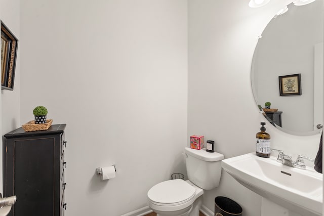 half bathroom featuring toilet, baseboards, and a sink