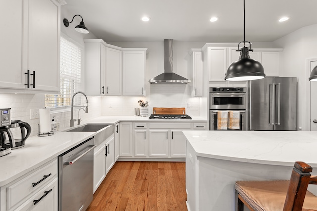 kitchen with stainless steel appliances, a sink, white cabinetry, decorative backsplash, and wall chimney range hood