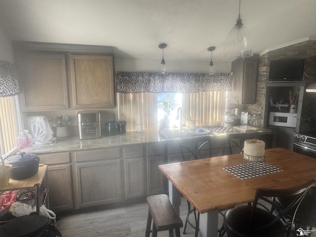 kitchen featuring light wood finished floors, a sink, light countertops, white microwave, and hanging light fixtures