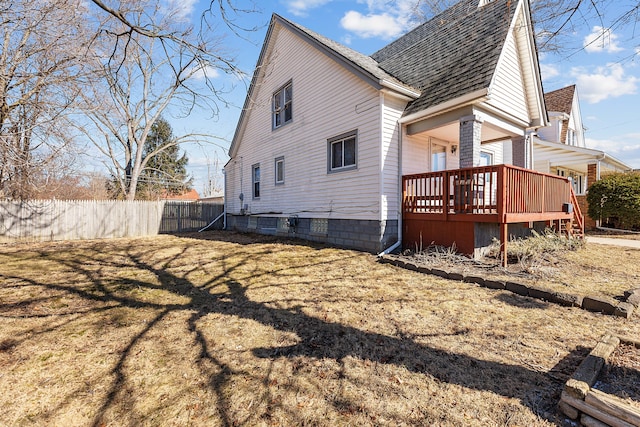 rear view of house with a deck, fence, a lawn, and a shingled roof