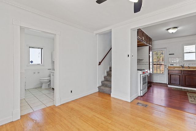 unfurnished living room featuring visible vents, stairs, light wood-type flooring, ornamental molding, and a sink