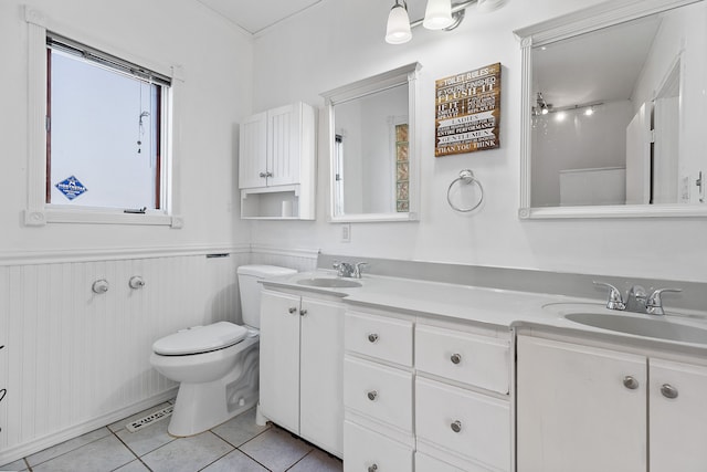 full bath with double vanity, a sink, wainscoting, tile patterned floors, and toilet